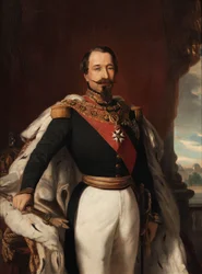 Napoleon III. in Uniform mit Hermelinmantel an einem Tisch mit Krone und Zepter, im Hintergrund der Louvre